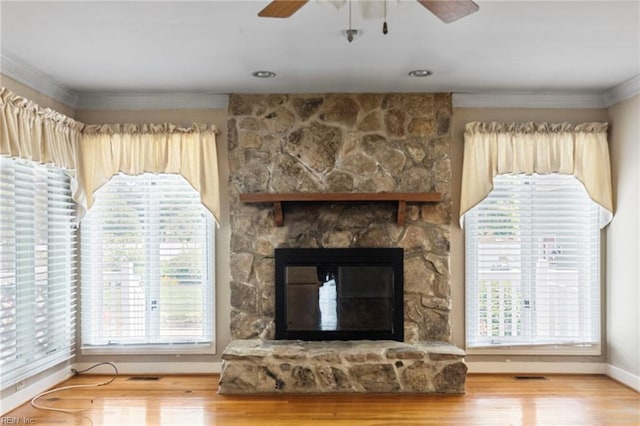 unfurnished living room with ceiling fan, baseboards, wood finished floors, crown molding, and a stone fireplace