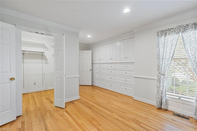 unfurnished bedroom featuring crown molding, light wood-style flooring, baseboards, recessed lighting, and a walk in closet