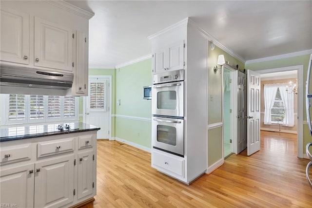 kitchen featuring stainless steel double oven, light wood-style floors, under cabinet range hood, baseboards, and healthy amount of natural light