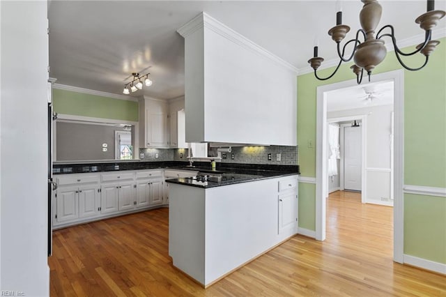 kitchen with a peninsula, decorative backsplash, white cabinetry, a chandelier, and crown molding