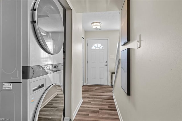 washroom featuring estacked washer and dryer, dark wood-style floors, and baseboards