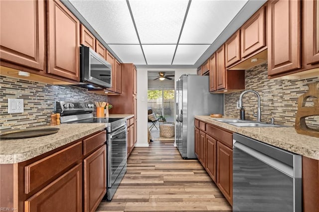 kitchen with appliances with stainless steel finishes, a sink, a ceiling fan, light wood-style flooring, and light countertops