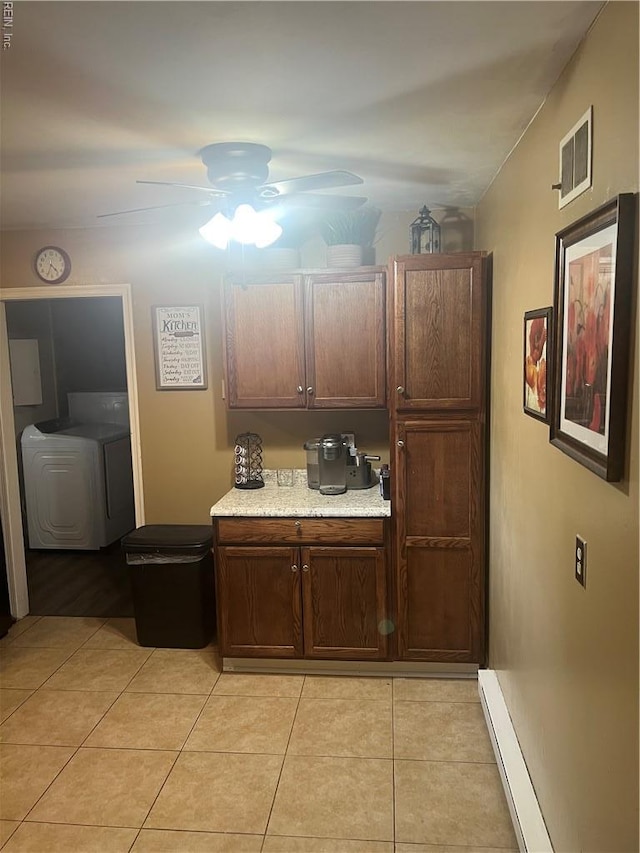 kitchen featuring ceiling fan, light countertops, washing machine and dryer, light tile patterned floors, and a baseboard radiator