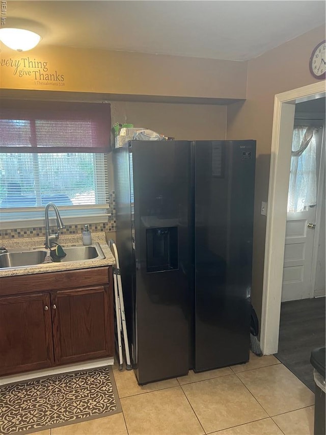 kitchen with a sink, black refrigerator with ice dispenser, light tile patterned floors, light countertops, and dark brown cabinets