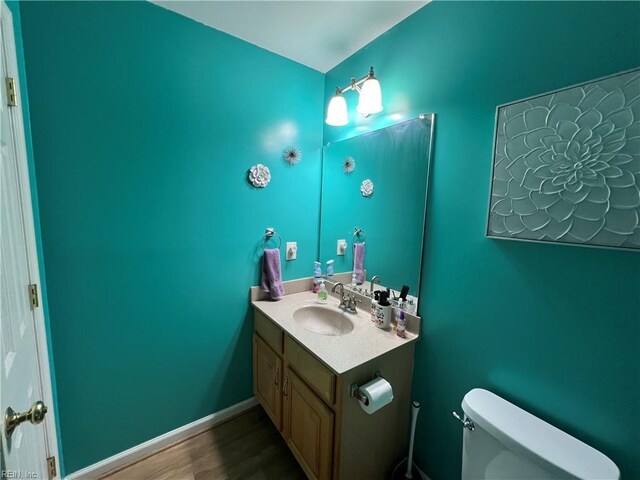 half bathroom featuring wood finished floors, toilet, and vanity