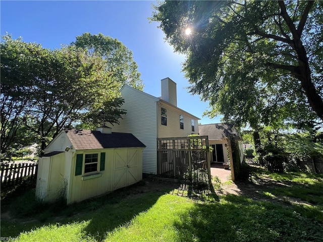 rear view of property with a shed, fence, an outbuilding, a chimney, and a wooden deck