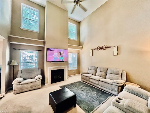carpeted living room featuring a towering ceiling, a fireplace, plenty of natural light, and a ceiling fan