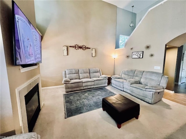carpeted living area with a towering ceiling, arched walkways, a glass covered fireplace, and baseboards