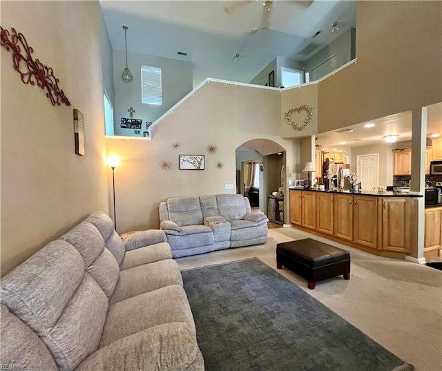 living room featuring a towering ceiling, arched walkways, light colored carpet, and ceiling fan