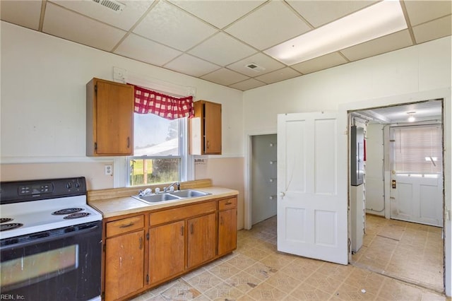 kitchen featuring electric stove, a sink, a drop ceiling, light countertops, and brown cabinetry