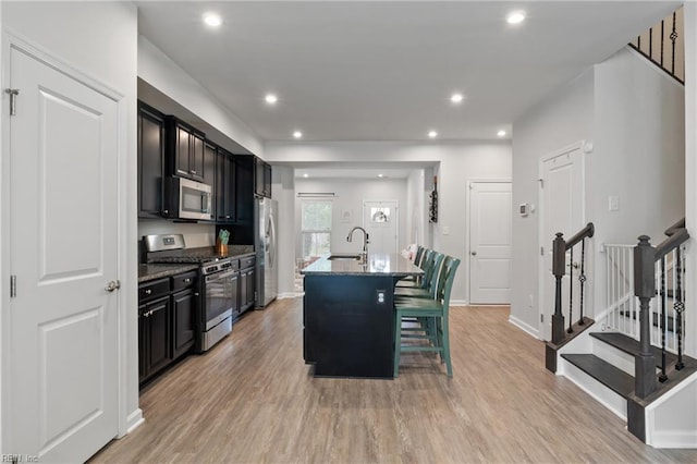 705 Mapleleaf Ln, Virginia Beach, VA 23462 - kitchen with stainless steel appliances, dark cabinetry, light wood-type flooring, a kitchen island with sink, and a kitchen bar