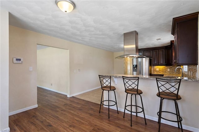 2212 Wildwood Rd, Chesapeake, VA 23323 - kitchen featuring island exhaust hood, stainless steel refrigerator with ice dispenser, dark brown cabinetry, a peninsula, and light stone counters
