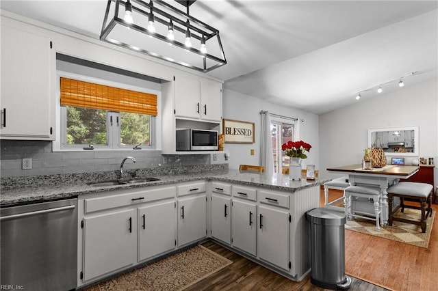kitchen featuring appliances with stainless steel finishes, a sink, a peninsula, decorative backsplash, and dark wood-type flooring