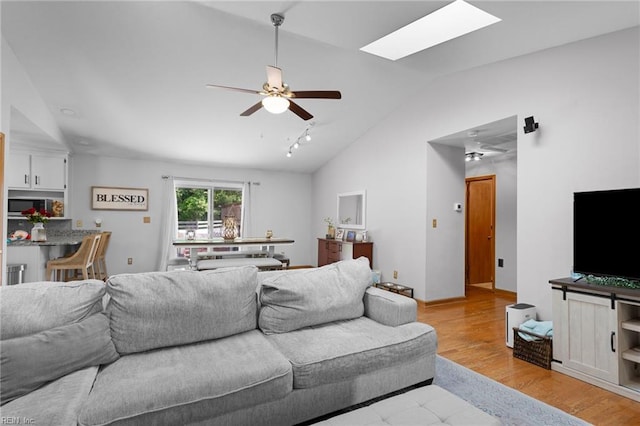 living room with lofted ceiling, ceiling fan, a skylight, and light wood finished floors