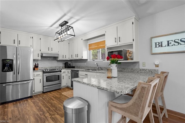 kitchen featuring appliances with stainless steel finishes, a sink, under cabinet range hood, a peninsula, and white cabinetry