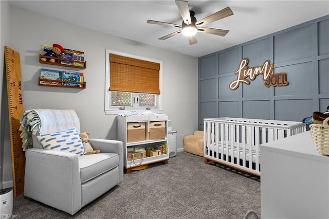 bedroom with a crib, carpet flooring, a decorative wall, and a ceiling fan