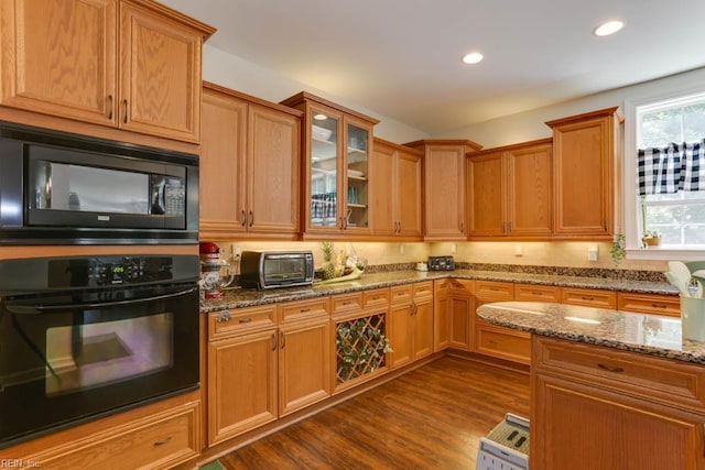 kitchen featuring black appliances, stone countertops, glass insert cabinets, dark wood-type flooring, and recessed lighting