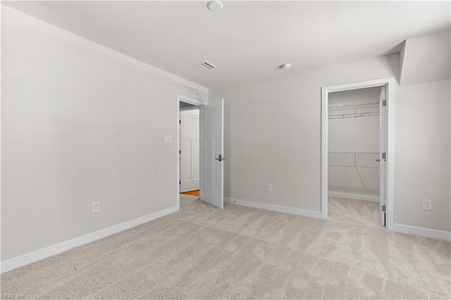 unfurnished bedroom with light carpet, a spacious closet, baseboards, and a closet