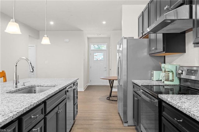 kitchen featuring stainless steel appliances, under cabinet range hood, light wood-style flooring, a sink, and pendant lighting