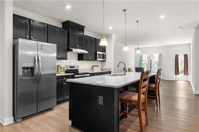kitchen featuring appliances with stainless steel finishes, a sink, under cabinet range hood, dark cabinetry, and recessed lighting