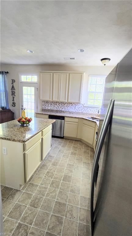 kitchen with stainless steel appliances, plenty of natural light, cream cabinetry, light stone counters, and recessed lighting