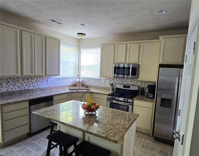 kitchen with appliances with stainless steel finishes, a sink, tasteful backsplash, a kitchen bar, and light stone counters