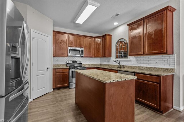 3001 Ravine Gap Dr, Suffolk, VA 23434 - kitchen with appliances with stainless steel finishes, light wood-style floors, tasteful backsplash, a center island, and light stone countertops