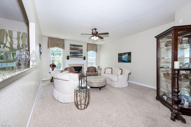 carpeted living area featuring baseboards, ceiling fan, and a fireplace