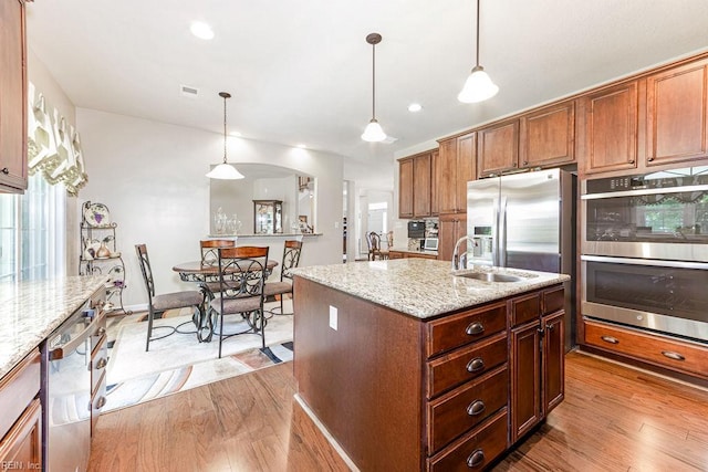 kitchen featuring stainless steel appliances, a sink, light wood finished floors, light stone countertops, and pendant lighting
