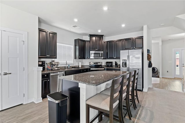 230 Independence St, Portsmouth, VA 23701 - kitchen with appliances with stainless steel finishes, a kitchen island, a breakfast bar, light wood-type flooring, and dark stone counters