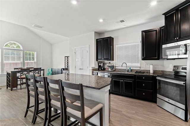 230 Independence St, Portsmouth, VA 23701 - kitchen featuring stainless steel appliances, dark cabinetry, a sink, a breakfast bar area, and light wood-style floors