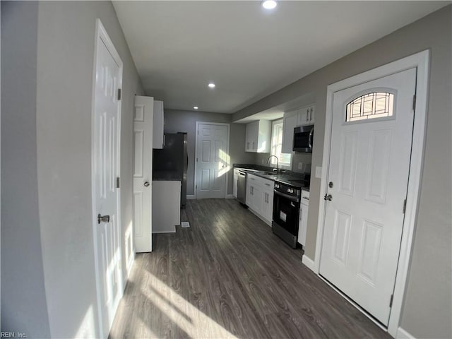 kitchen featuring appliances with stainless steel finishes, a sink, dark wood finished floors, white cabinets, and baseboards