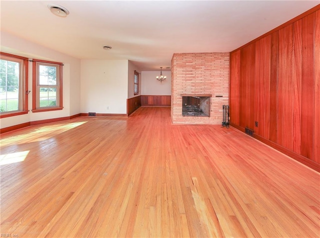 101 Elmhurst Ln, Portsmouth, VA 23701 - unfurnished living room featuring light wood-style floors, a chandelier, wooden walls, a fireplace, and baseboards