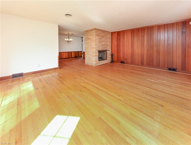 101 Elmhurst Ln, Portsmouth, VA 23701 - unfurnished living room featuring a chandelier, light wood finished floors, a brick fireplace, wooden walls, and baseboards