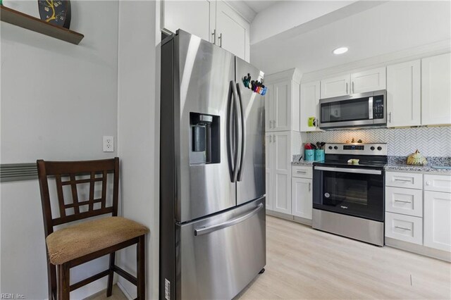 611 74th St, Newport News, VA 23605 - kitchen featuring stainless steel appliances, white cabinets, backsplash, light wood finished floors, and light stone countertops
