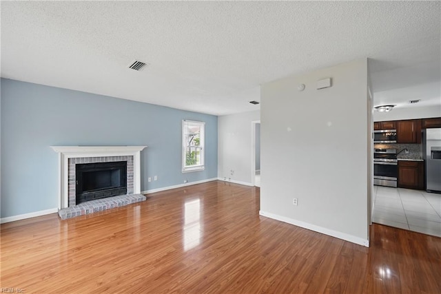 1405 Collingswood Trl, Virginia Beach, VA 23464 - unfurnished living room featuring light wood-style floors, a textured ceiling, a brick fireplace, and baseboards