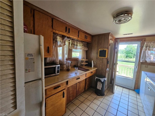 1428 24th St, Newport News, VA 23607 - kitchen with stainless steel microwave, freestanding refrigerator, washing machine and clothes dryer, light tile patterned flooring, and brown cabinetry