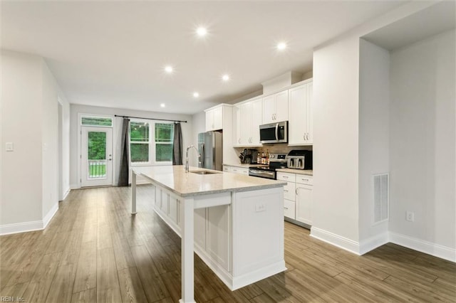 1544 Stanford Ln, Newport News, VA 23608 - kitchen featuring appliances with stainless steel finishes, a spacious island, white cabinets, light wood finished floors, and a breakfast bar