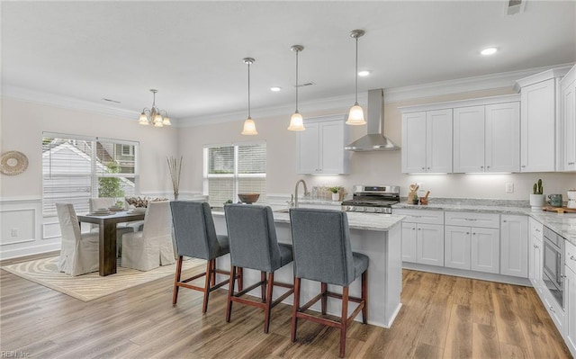 1608 Holland Ave, Norfolk, VA 23509 - kitchen featuring wall chimney exhaust hood, appliances with stainless steel finishes, ornamental molding, white cabinets, and a kitchen bar