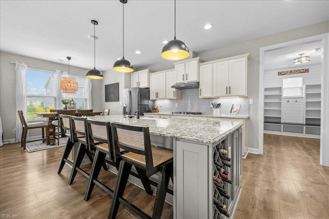 3012 George Starr Dr, Virginia Beach, VA 23456 - kitchen featuring under cabinet range hood, appliances with stainless steel finishes, tasteful backsplash, an island with sink, and a kitchen breakfast bar