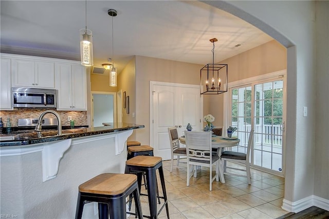 501 Beagle Gap Ct, Chesapeake, VA 23320 - kitchen featuring stainless steel microwave, arched walkways, a kitchen bar, dark stone counters, and decorative backsplash