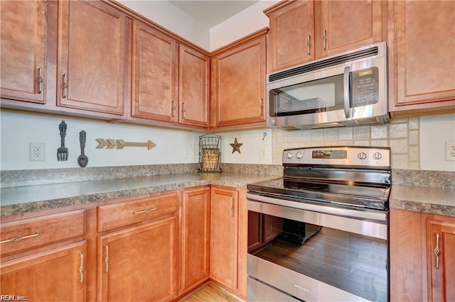 401 Blue Heron Trl, Carrollton, VA 23314 - kitchen featuring appliances with stainless steel finishes, brown cabinetry, and tasteful backsplash
