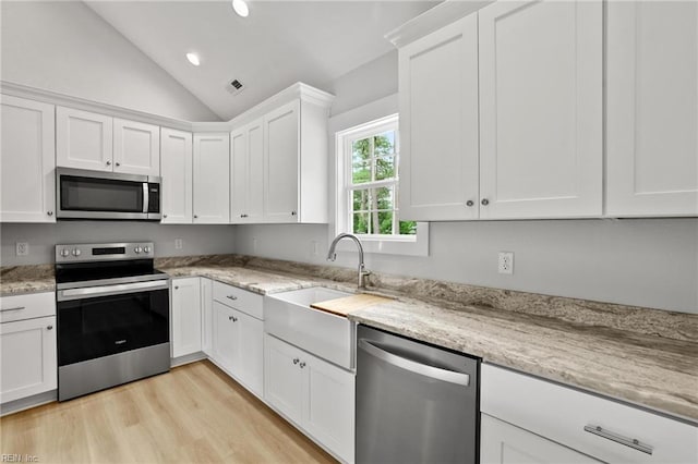1064 Tulls Creek Rd, Moyock, NC 27958 - kitchen featuring appliances with stainless steel finishes, vaulted ceiling, white cabinets, light wood-style floors, and light stone countertops