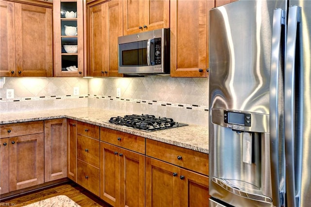 3907 Ethan Ln, Williamsburg, VA 23188 - kitchen featuring stainless steel appliances, brown cabinetry, light stone counters, and glass insert cabinets