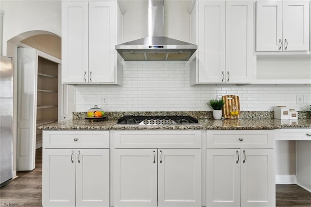 105 Brogden Ct, Hampton, VA 23666 - kitchen featuring wall chimney range hood, arched walkways, stainless steel gas cooktop, dark stone counters, and white cabinetry