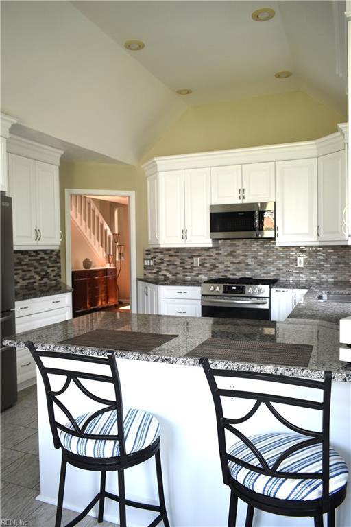 1176 Pond Cypress Dr, Virginia Beach, VA 23455 - kitchen featuring appliances with stainless steel finishes, lofted ceiling, decorative backsplash, white cabinetry, and a kitchen bar