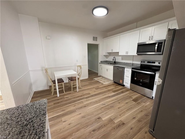 3711 Abingdon Cir, Norfolk, VA 23513 - kitchen featuring appliances with stainless steel finishes, light wood-style flooring, white cabinetry, dark stone countertops, and a sink