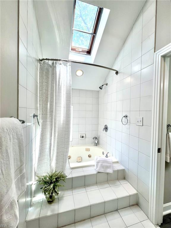30 Brough Ln # 301, Hampton, VA 23669 - bathroom featuring a skylight, a combined bath / shower with jetted tub, vaulted ceiling, tile walls, and tile patterned flooring