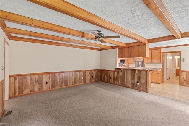 1118 Patrick Ln, Newport News, VA 23608 - unfurnished living room with beam ceiling, a ceiling fan, a wainscoted wall, light colored carpet, and wood walls