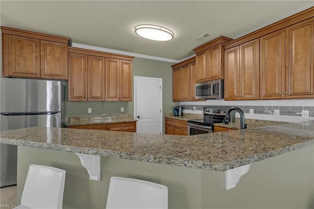7556 Villa Ct, Gloucester, VA 23061 - kitchen with appliances with stainless steel finishes, brown cabinetry, light stone counters, a breakfast bar area, and ornamental molding